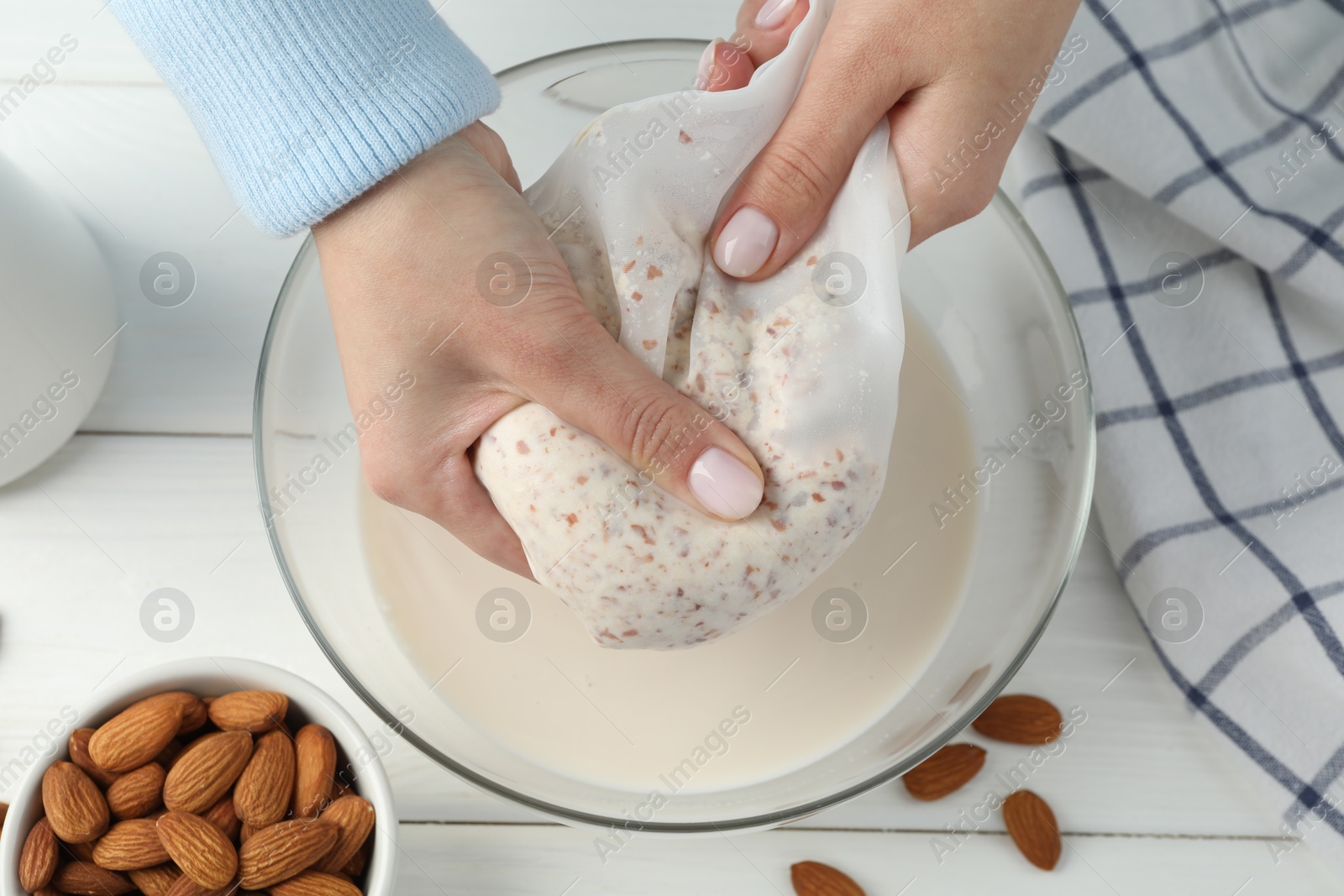 Photo of Woman making almond milk at white wooden table, top view