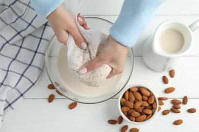 Woman making almond milk at white wooden table, top view