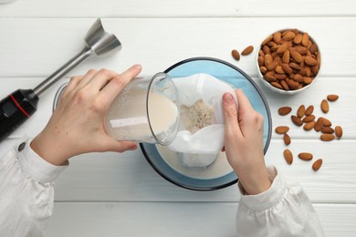 Photo of Woman making almond milk and nuts at white wooden table, top view