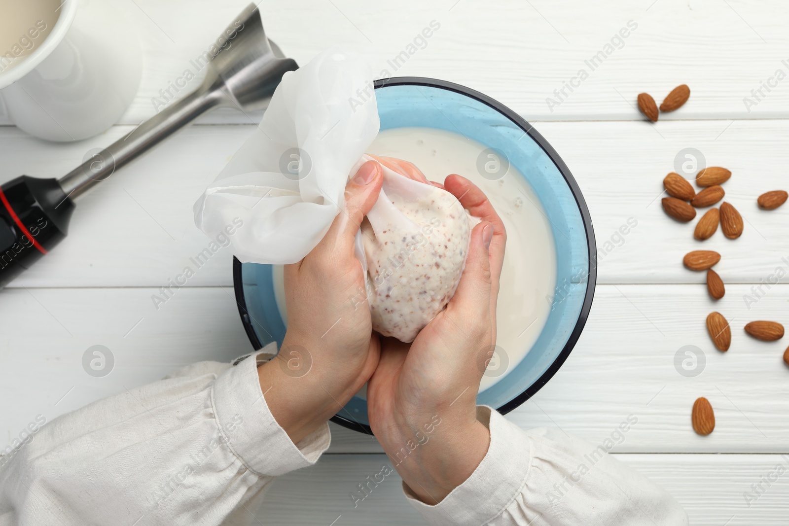 Photo of Woman making almond milk and nuts at white wooden table, top view