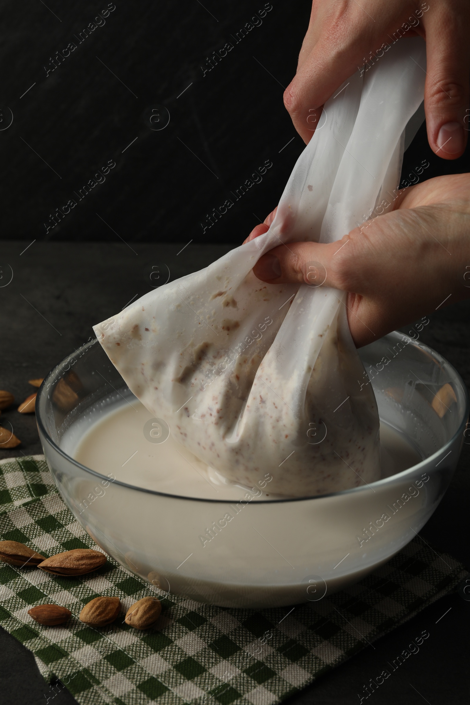 Photo of Woman making almond milk and nuts at black table, closeup