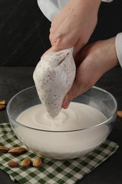 Woman making almond milk and nuts at black table, closeup