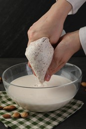 Woman making almond milk and nuts at black table, closeup