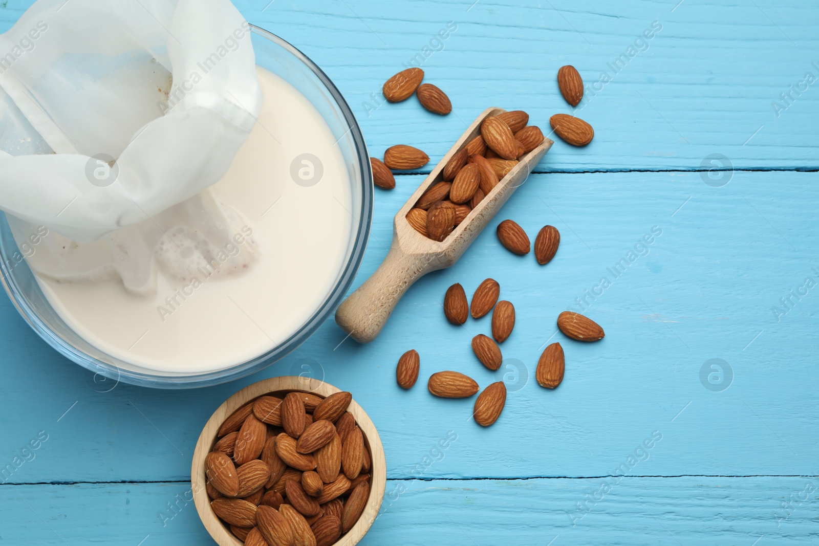 Photo of Homemade almond milk, cheesecloth with mixture and nuts on light blue wooden table, top view