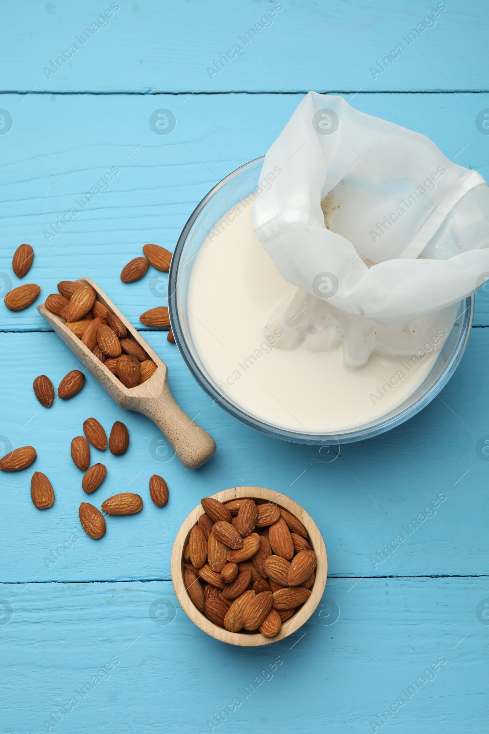 Photo of Homemade almond milk, cheesecloth with mixture and nuts on light blue wooden table, top view