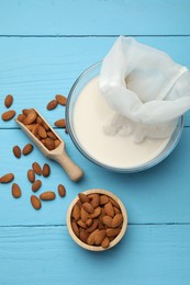 Homemade almond milk, cheesecloth with mixture and nuts on light blue wooden table, top view