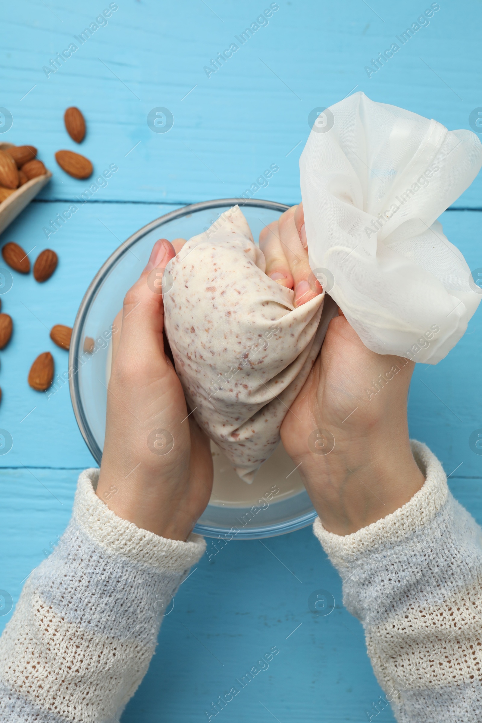 Photo of Woman making almond milk and nuts at light blue wooden table, top view