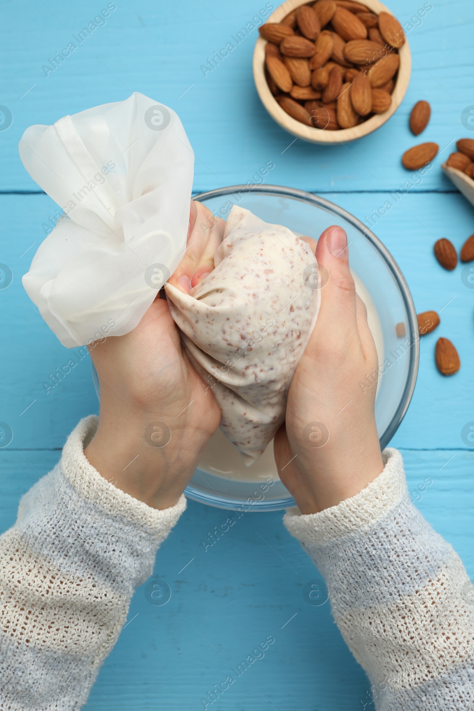 Photo of Woman making almond milk and nuts at light blue wooden table, top view