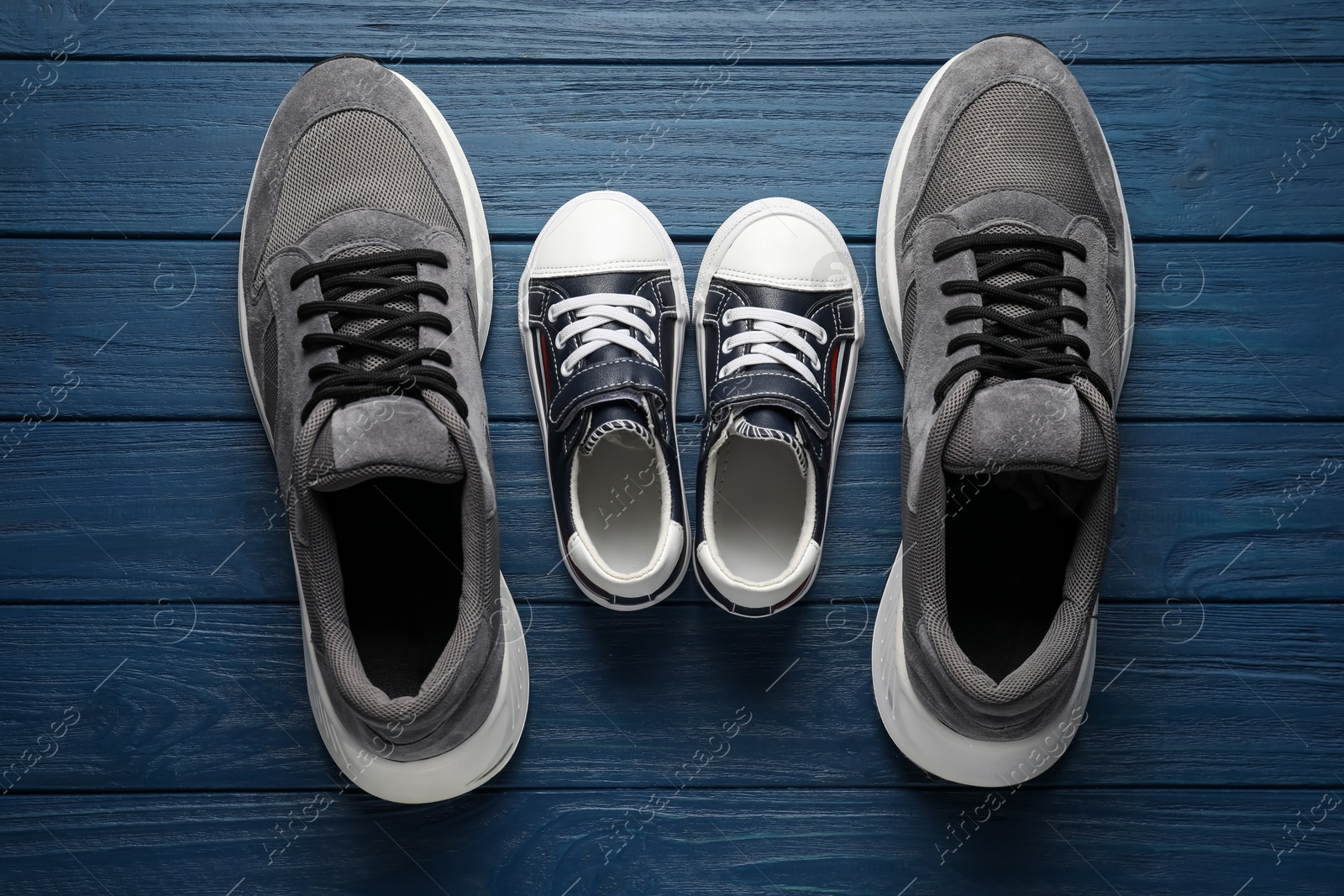 Photo of Big and small shoes on blue wooden table, top view