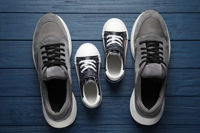 Photo of Big and small shoes on blue wooden table, top view