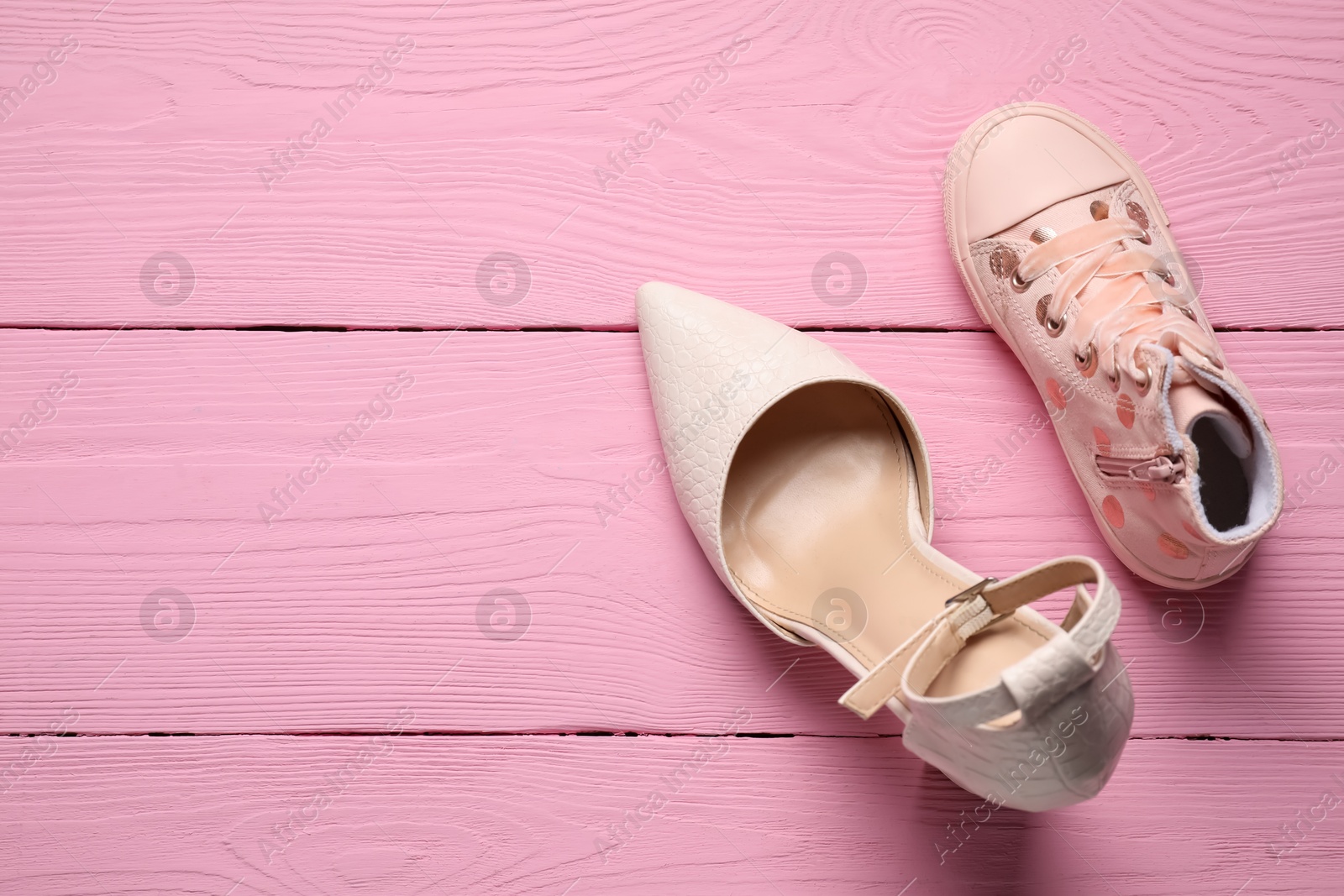 Photo of Big and small shoes on pink wooden table, top view. Space for text