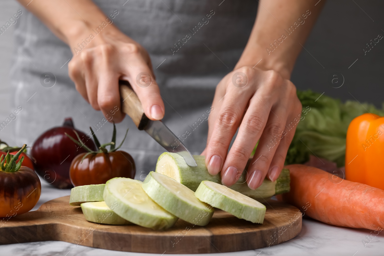 Photo of Cooking vegetable stew. Woman cutting zucchini at white marble table, closeup