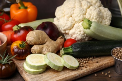 Photo of Cooking tasty stew. Fresh zucchini, ginger, tomatoes, cauliflower and peppercorns on wooden table