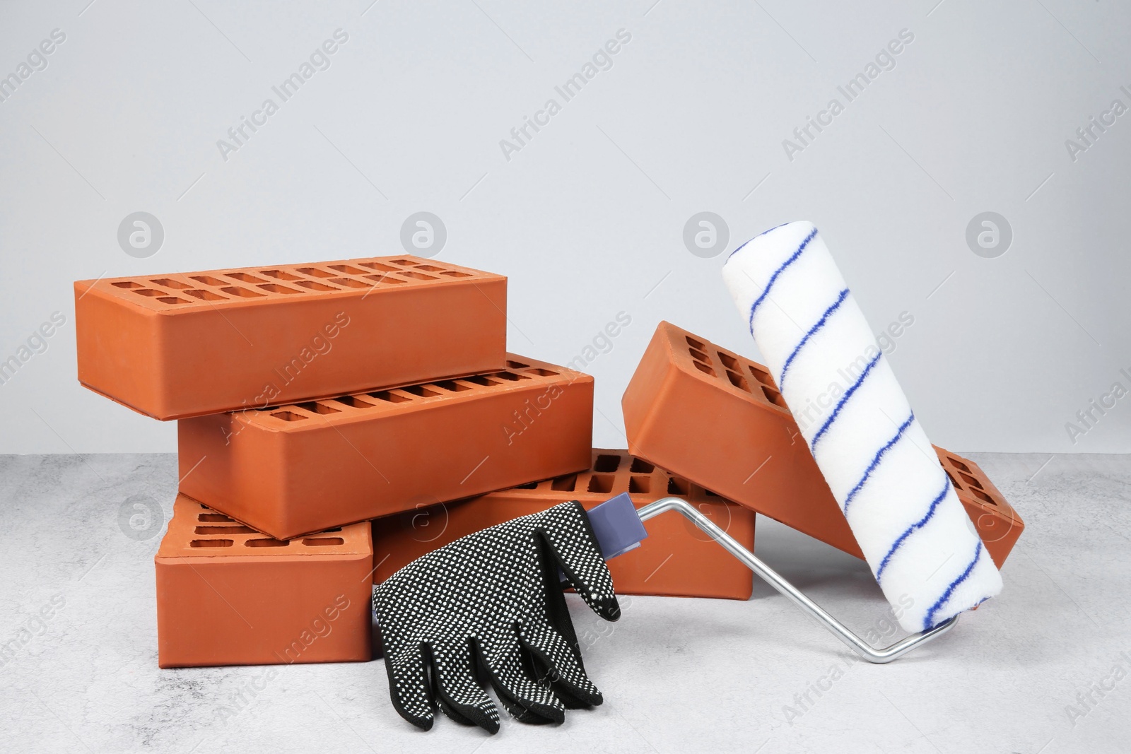 Photo of Red bricks, paint roller and glove on textured table against light background