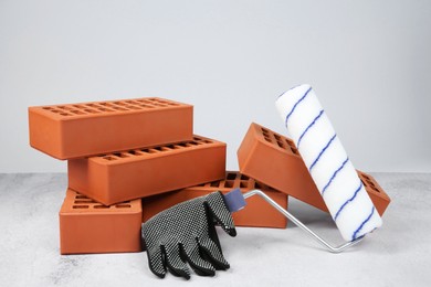 Red bricks, paint roller and glove on textured table against light background