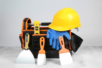 Photo of Bag for construction tools, building level, hard hat, glove and trowels on textured table against light background