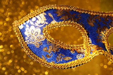 Photo of Beautiful carnival mask against blurred golden background, closeup