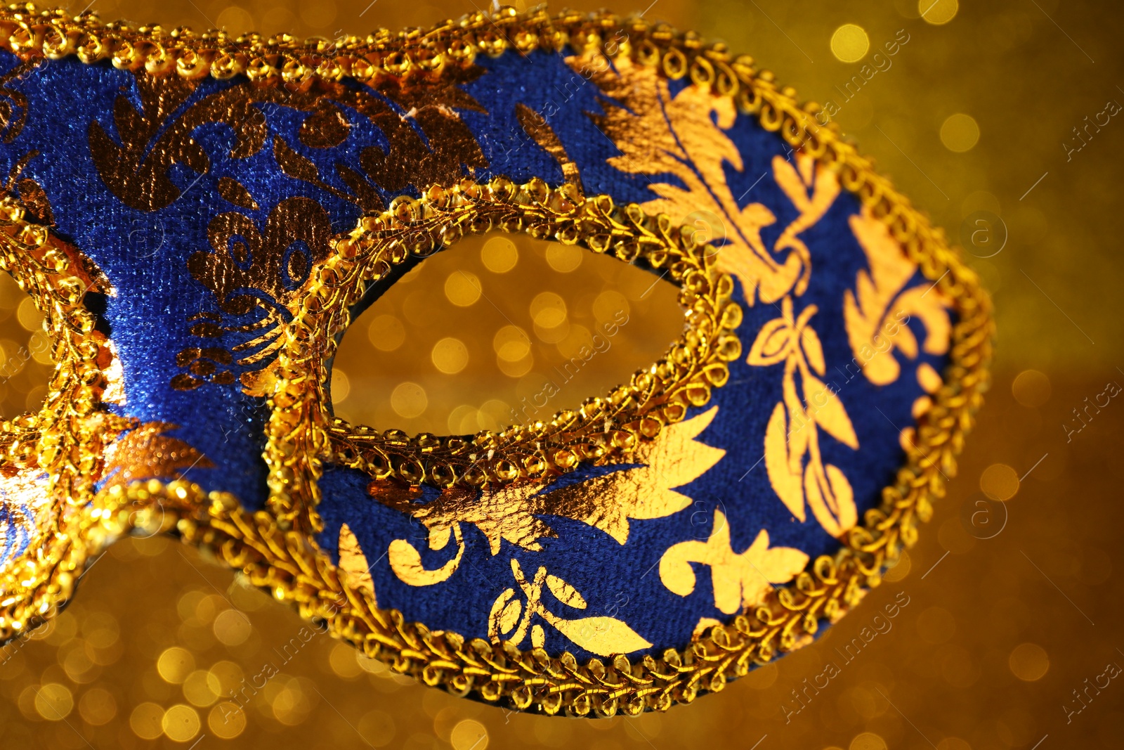 Photo of Beautiful carnival mask against blurred golden background, closeup