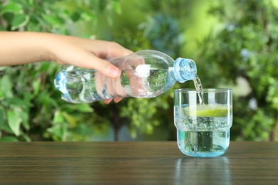 Photo of Woman pouring soda water from bottle into glass at wooden table, closeup