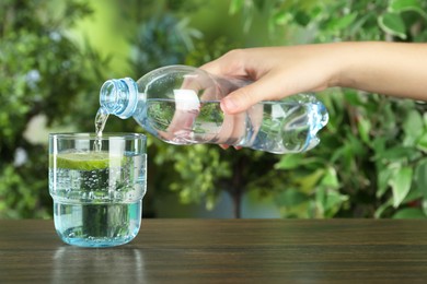 Photo of Woman pouring soda water from bottle into glass at wooden table, closeup