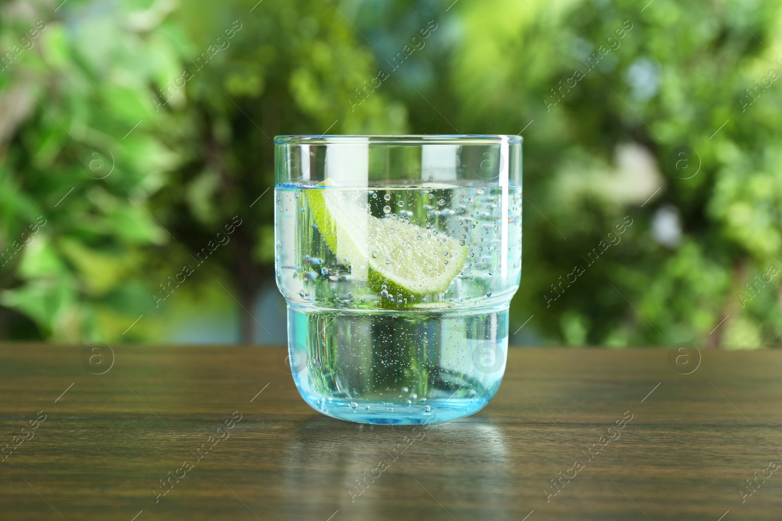 Photo of Glass of soda water with lime on wooden table against blurred background