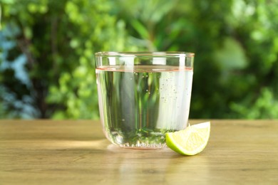 Photo of Glass of soda water with lime on wooden table against blurred background