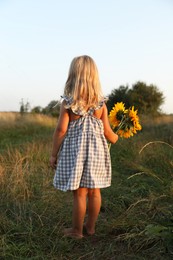 Photo of Little girl with sunflowers at meadow, back view. Child enjoying beautiful nature