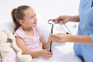 Photo of Doctor examining little girl on bed at hospital, closeup