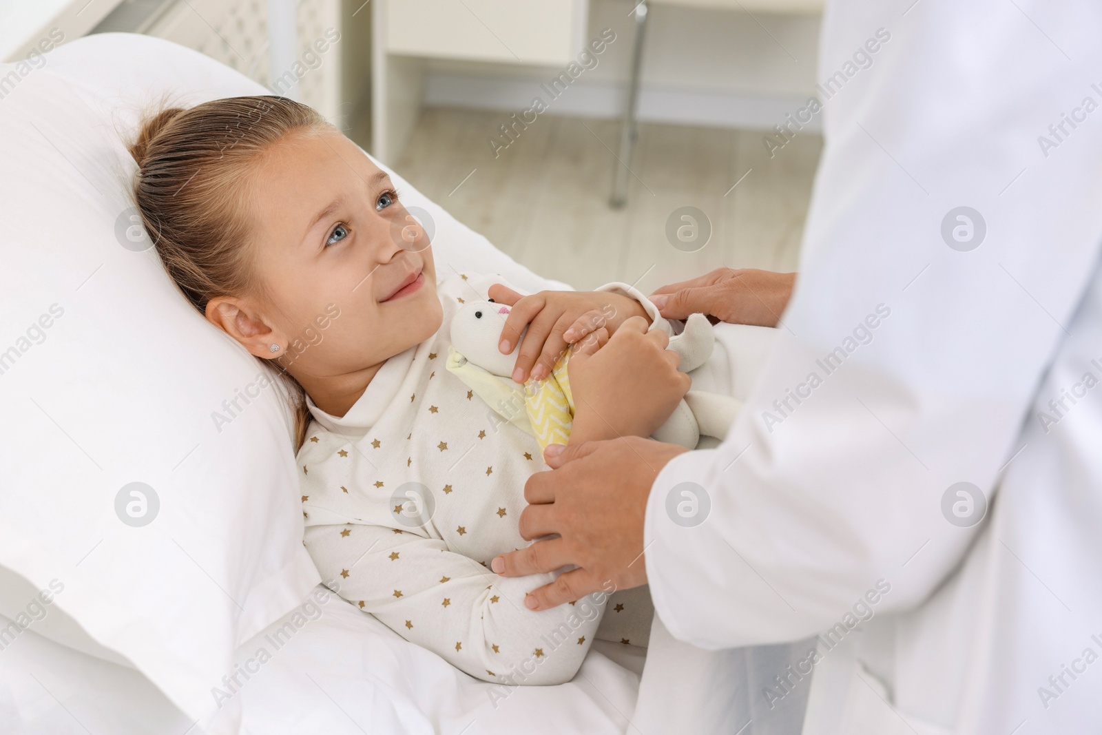 Photo of Doctor examining little girl on bed at hospital, closeup