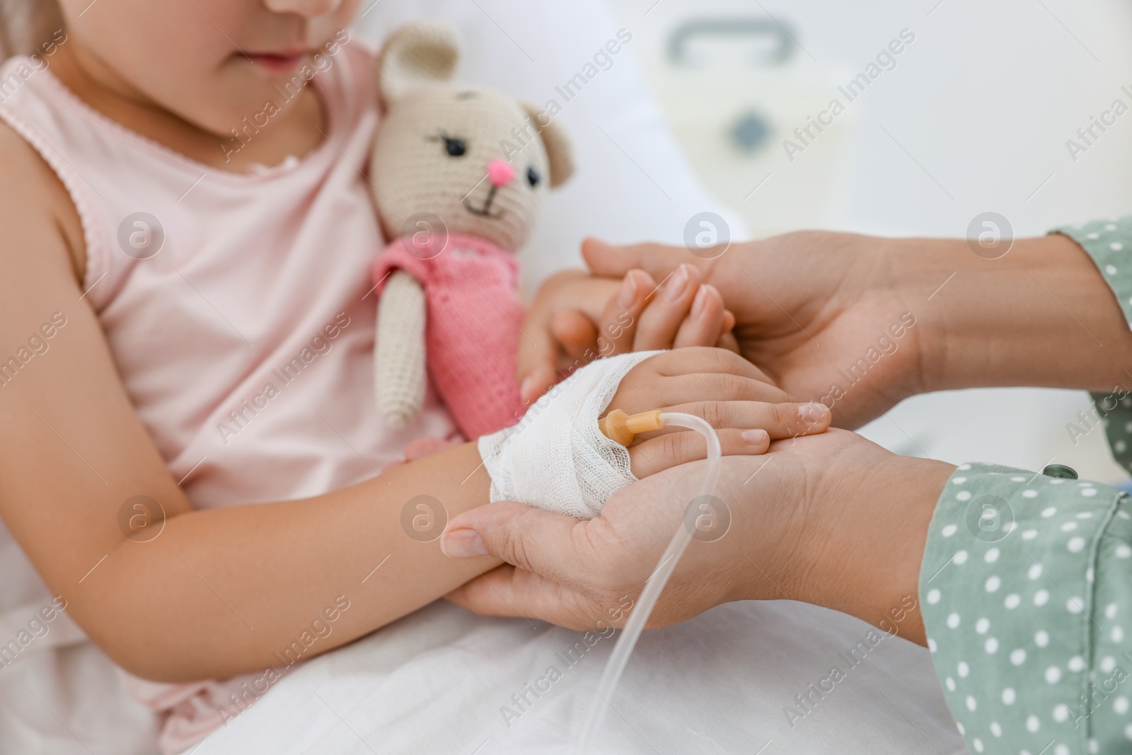 Photo of Mother and her little daughter with IV drip on bed in hospital, closeup