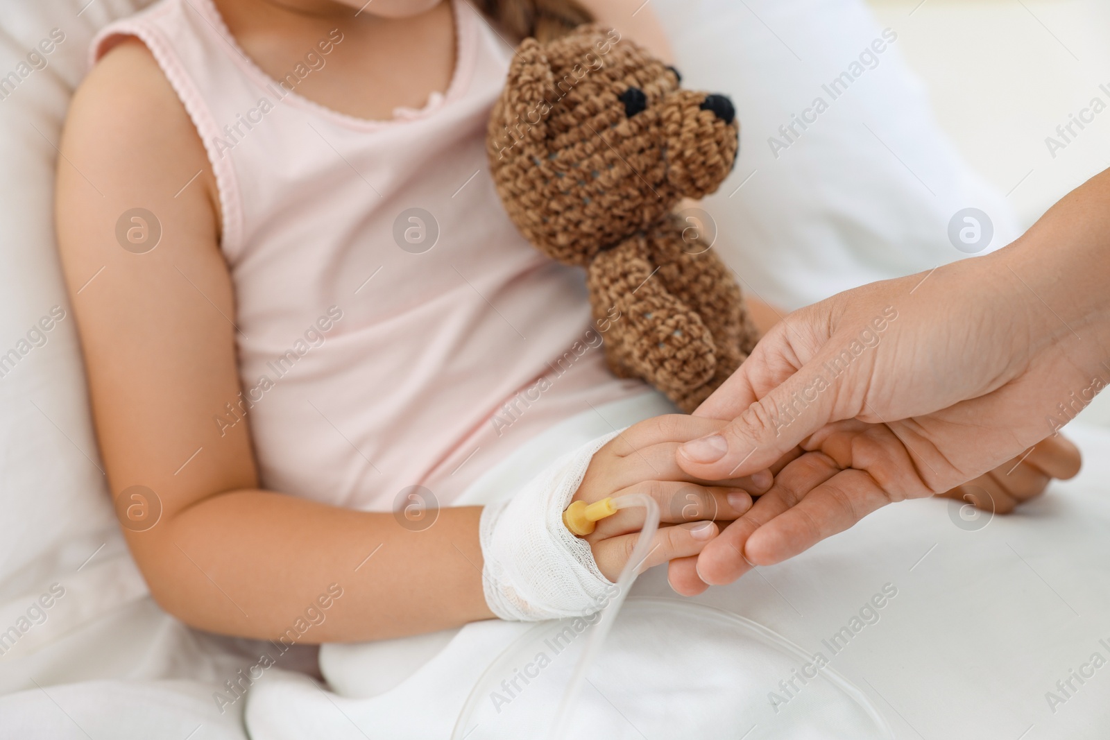 Photo of Mother and her little daughter with IV drip on bed in hospital, closeup