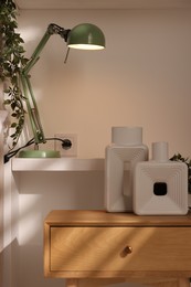 Photo of Beautiful vases on bedside table and lamp in room