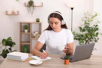 Photo of Student taking notes while studying at wooden table indoors