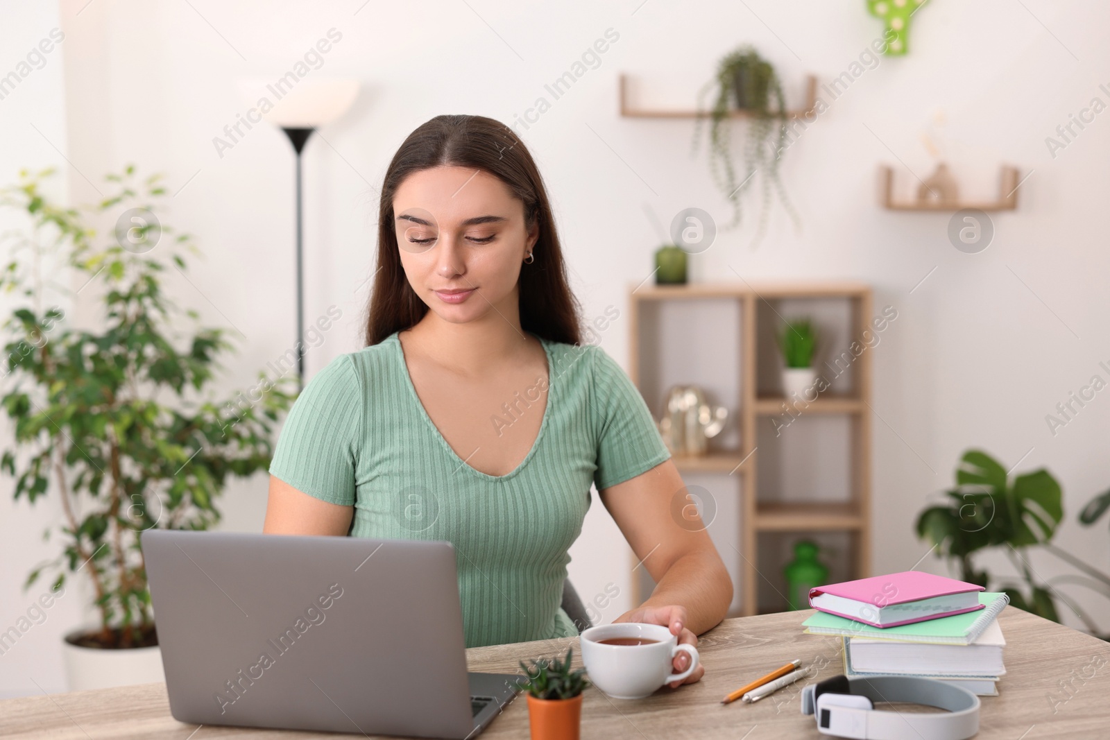 Photo of Student with cup of drink studying at wooden table indoors