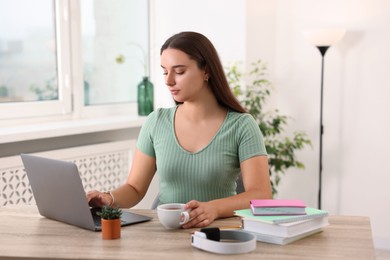 Student with cup of drink studying at wooden table indoors