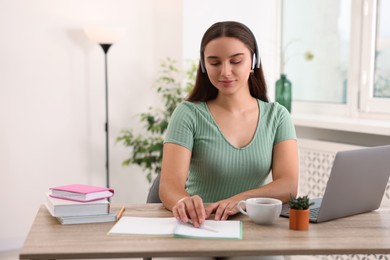 Photo of Student in headphones studying at wooden table indoors