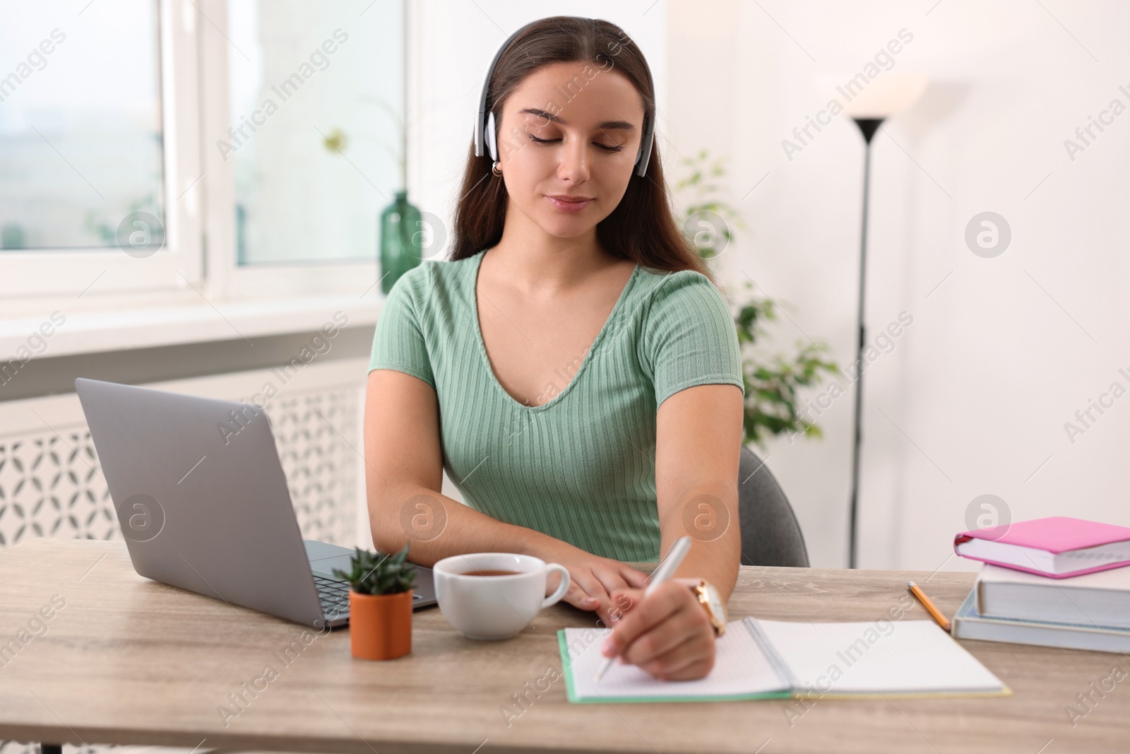 Photo of Student in headphones studying at wooden table indoors