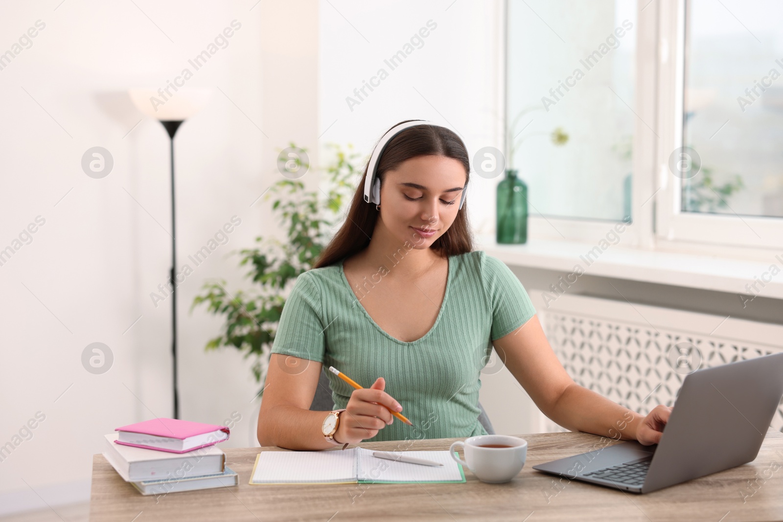 Photo of Student in headphones studying at wooden table indoors