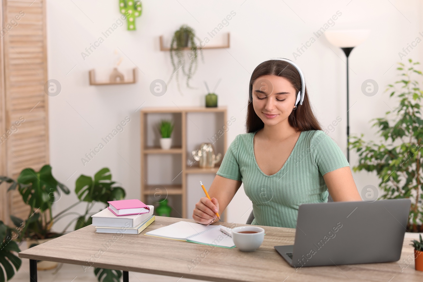 Photo of Student in headphones studying at wooden table indoors