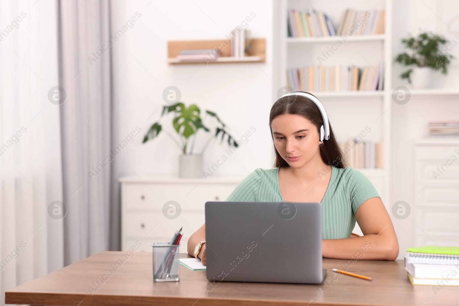 Photo of Student in headphones studying with laptop at wooden table indoors