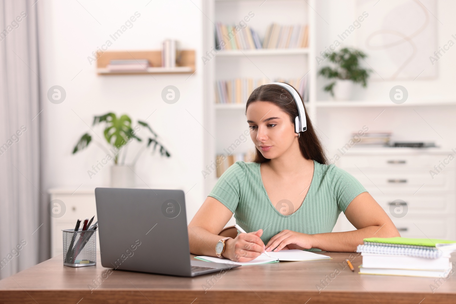 Photo of Student in headphones studying at wooden table indoors