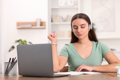 Photo of Student in headphones studying at wooden table indoors