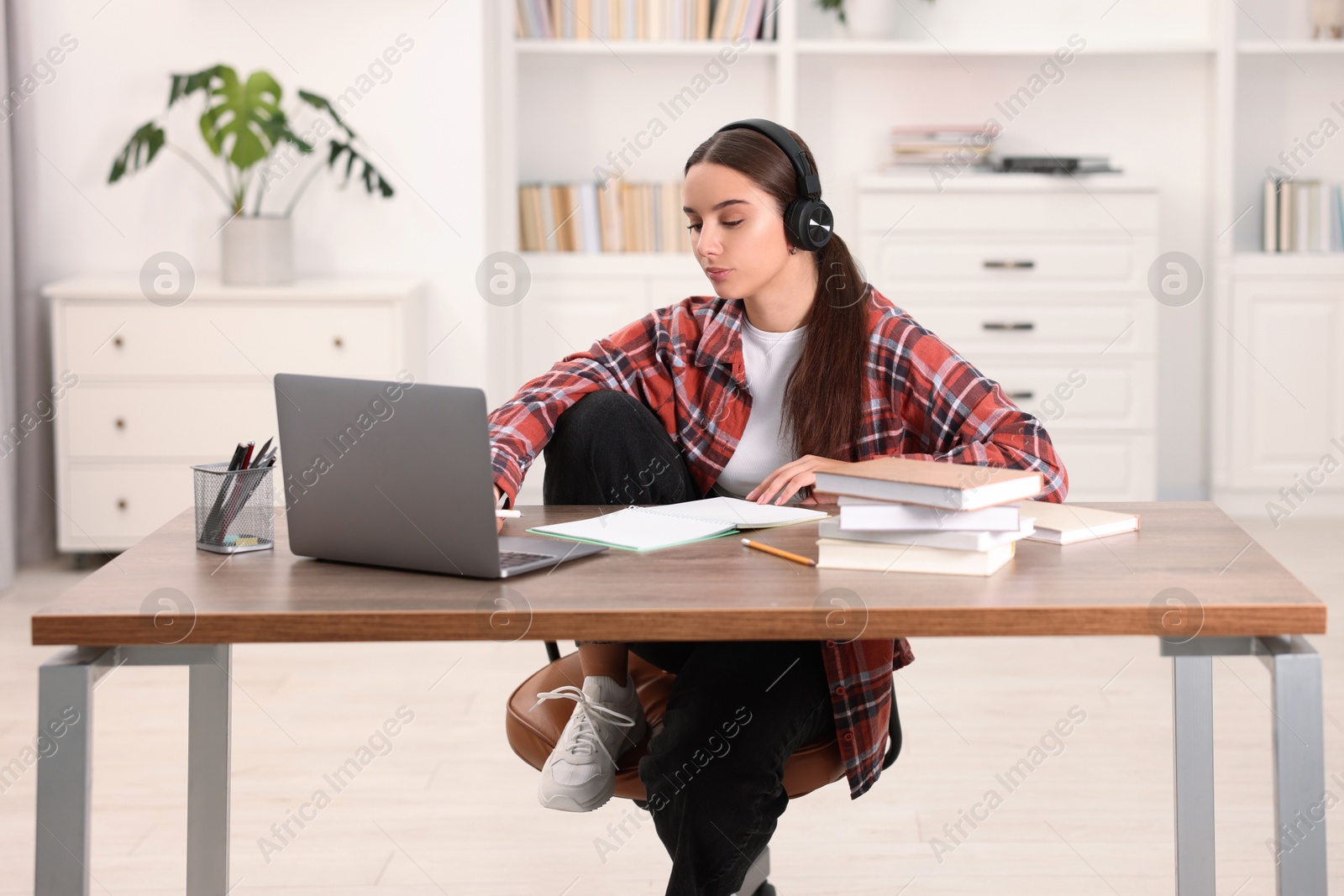 Photo of Student in headphones studying with laptop at wooden table indoors