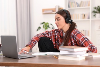 Photo of Student in headphones studying with laptop at wooden table indoors