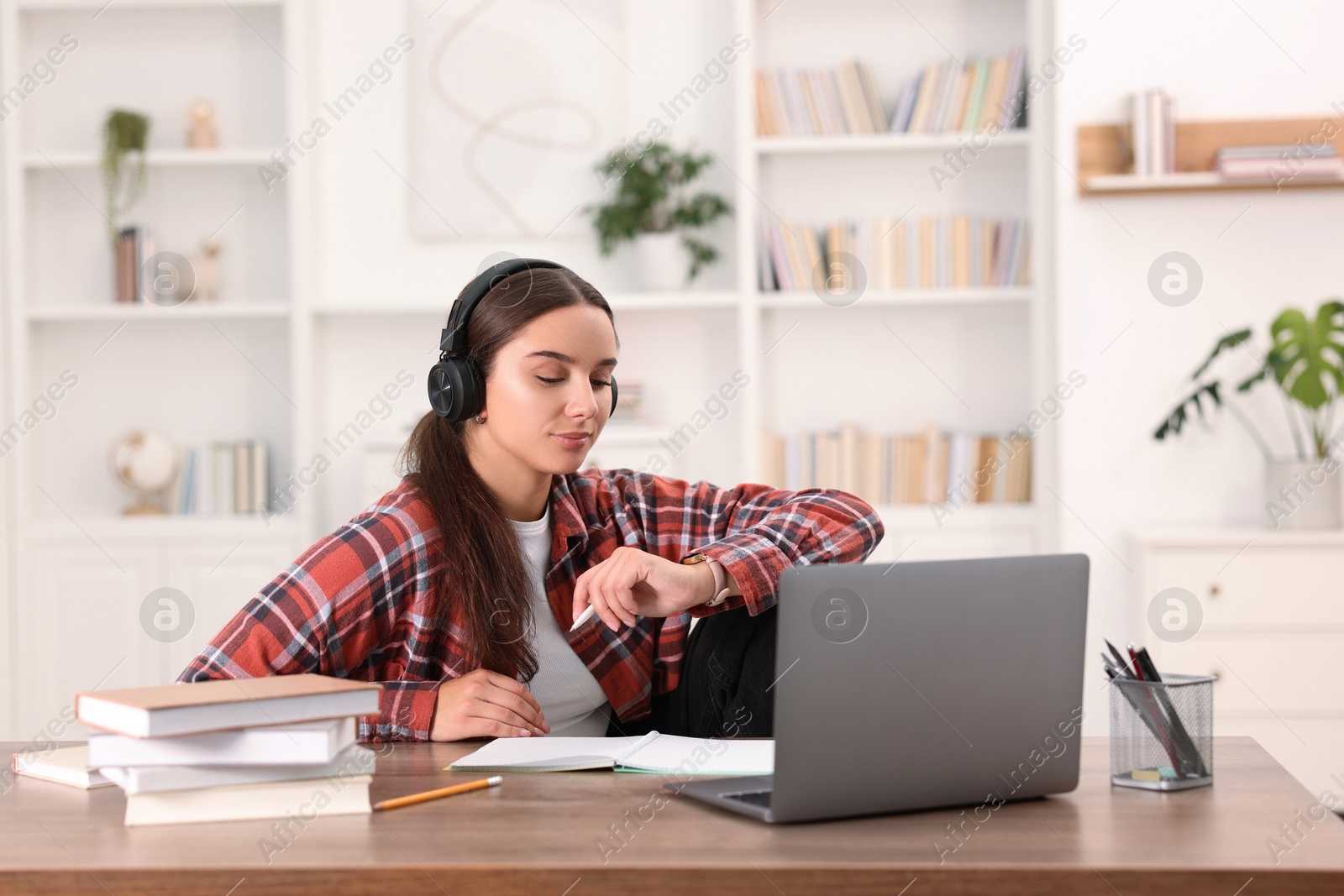 Photo of Student in headphones studying at wooden table indoors