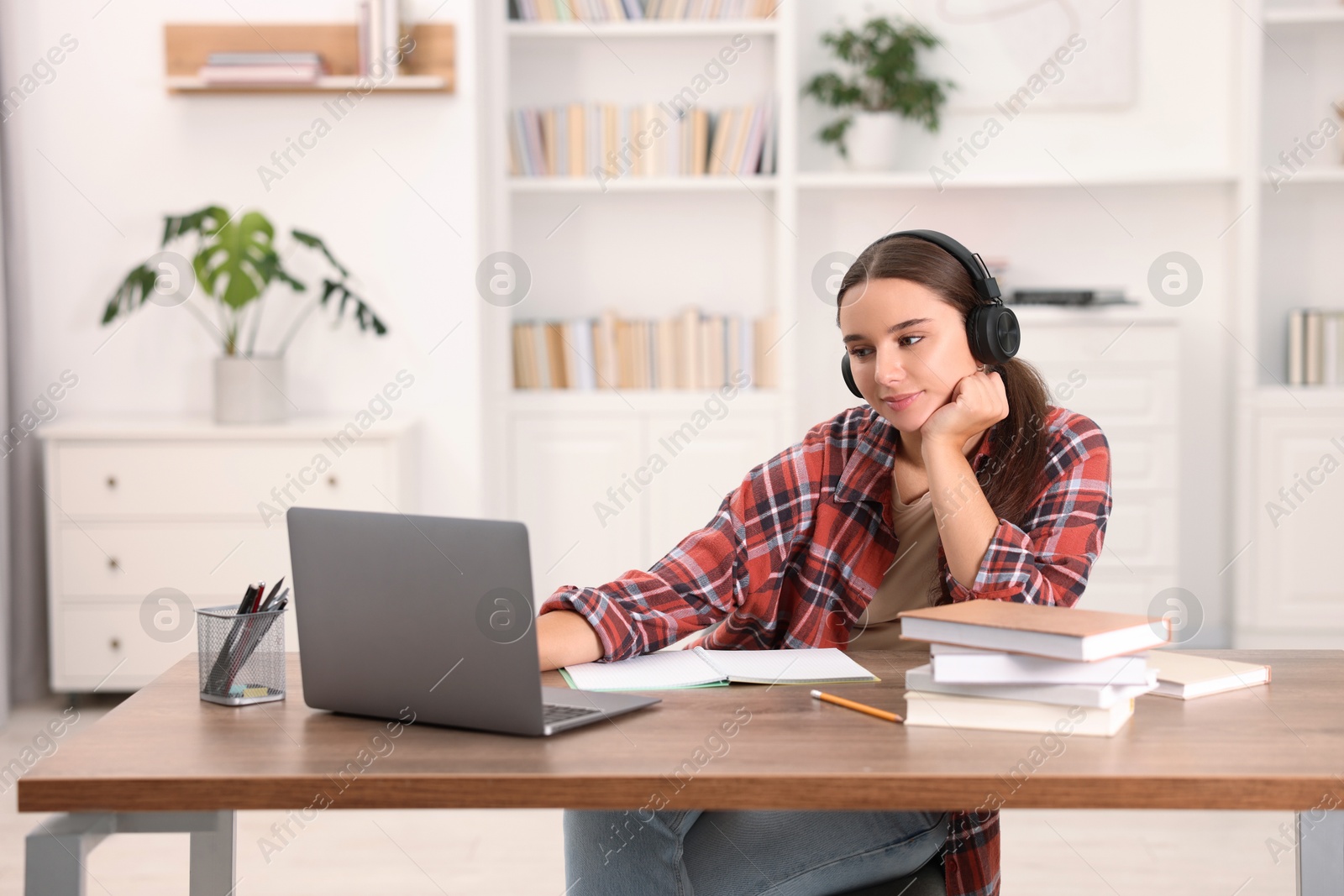 Photo of Student in headphones studying with laptop at wooden table indoors