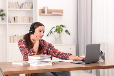 Photo of Student in headphones studying with laptop at wooden table indoors