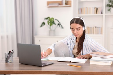 Photo of Student in headphones studying at wooden table indoors