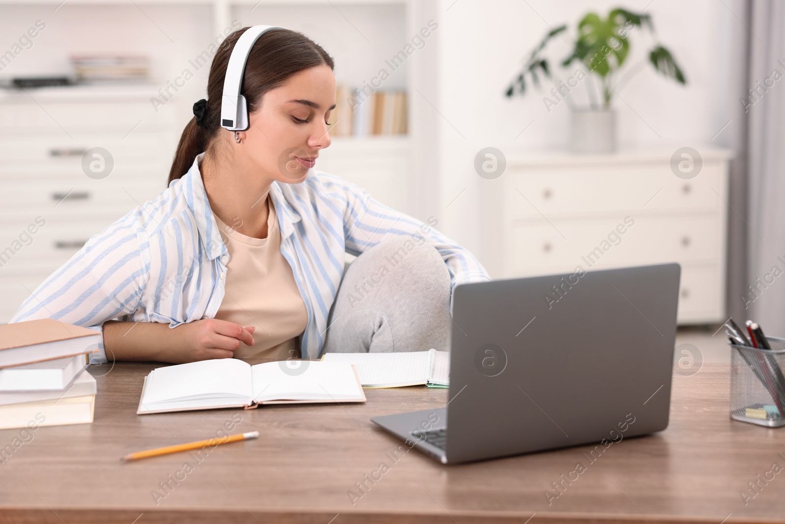 Photo of Student in headphones studying at wooden table indoors