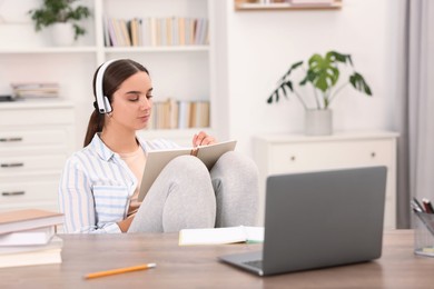 Photo of Student in headphones taking notes while studying indoors